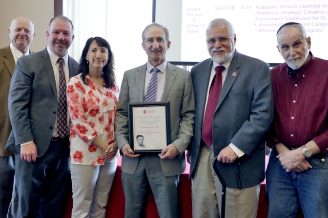 Male holding award with other University administrators