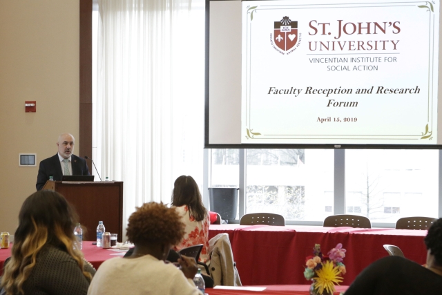Male at podium speaking to audience with powerpoint on screen