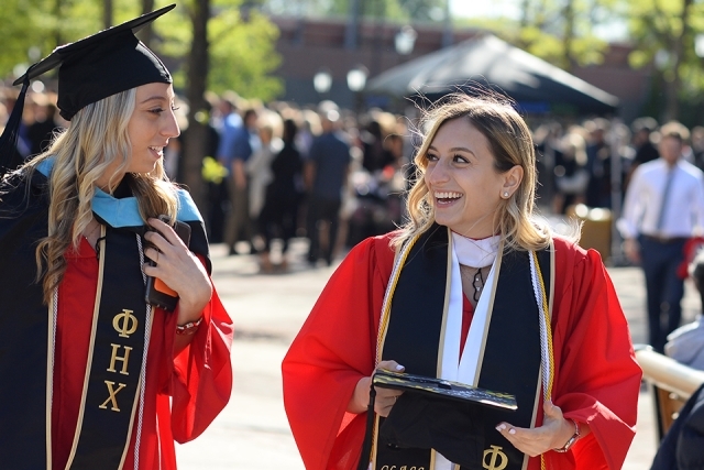 Two female students smiling at each other in commencement attire