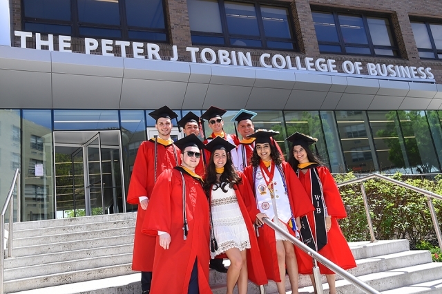 Group of students standing infront of the Peter J. Tobin College of Business school in their academic attire