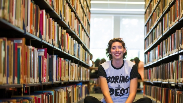 female student sitting on floor between library shelves