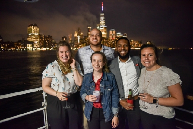 Group of alumni posing for photo on boat with statue of liberty in the background