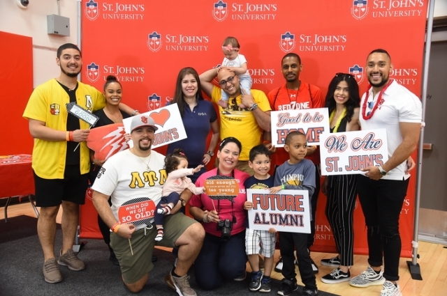 Group of people posing infront of step and repeat holding signs at Alumni weekend