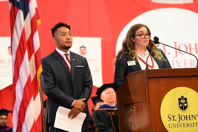 Two students speaking at podium with American flag next to them