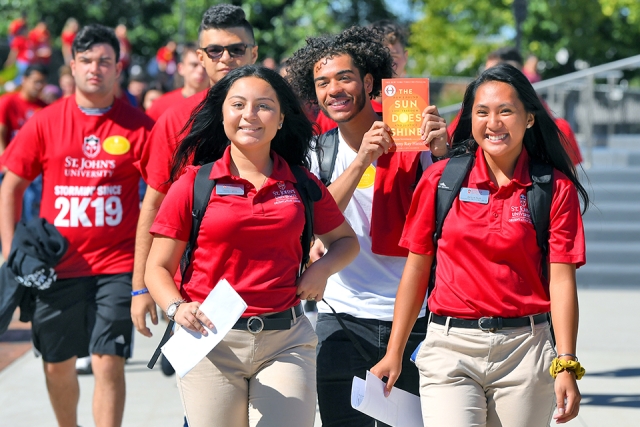 Group of students walking on campus while waving at the camera