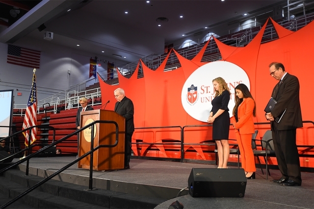 Father Tracey at podium leading opening prayer