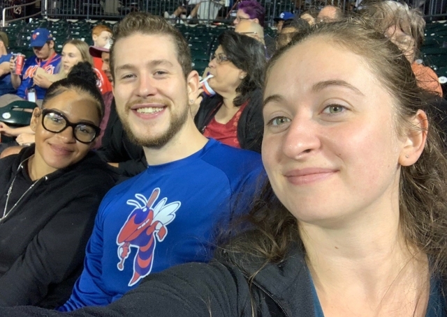 Three people sitting in stands at baseball field