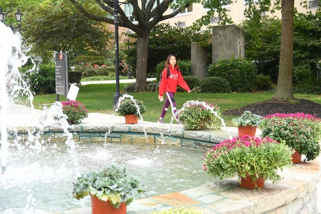 Student in SJU sweatshirt walks past fountain