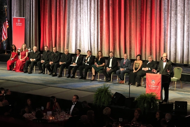 Man at podium onstage; President Gempesaw, guests and honorees are seated onstage behind him