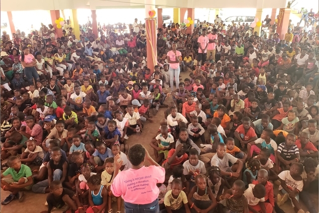 Group of students sitting on the ground listening to a female speak