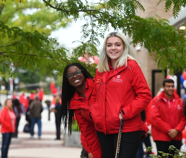 admissions ambassadors on campus looking at the camera, two female wearing red jackets standing outside.