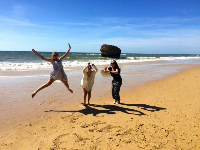3 people jump for a photo on a sandy beach