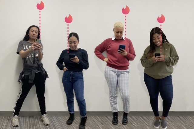 Four females standing next to each other as they look at their phones