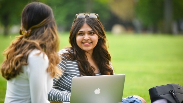 Two female students talking to each other while outside on laptops