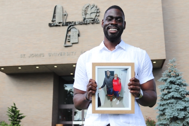 St. John's Law student Matthew Atewe standing in front of the Law School and holding a photo of him and his father