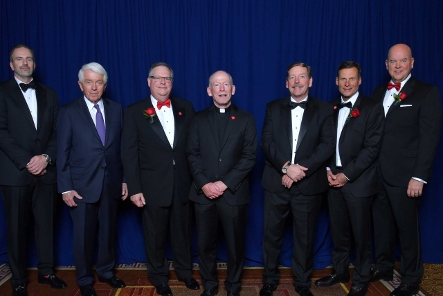 7 males standing infront of blue backdrop posing for photo