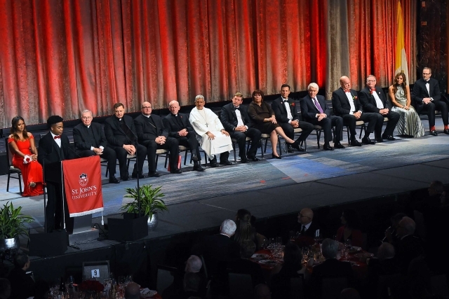 group shot of people sitting on stage while one male speaks at poidum