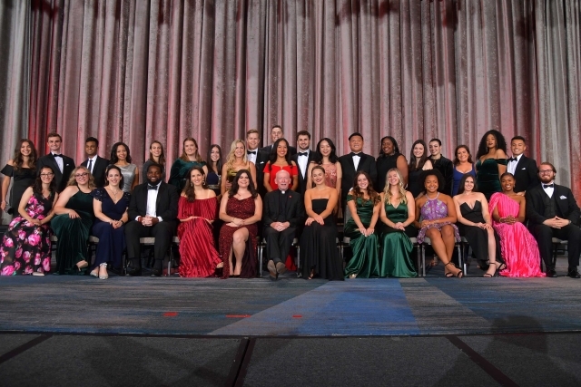 Large group of students sitting on stage posing for photo