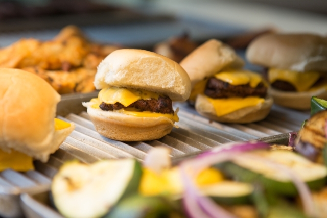 A grill with vegetables out of focus, cheeseburger sliders, and chicken fingers