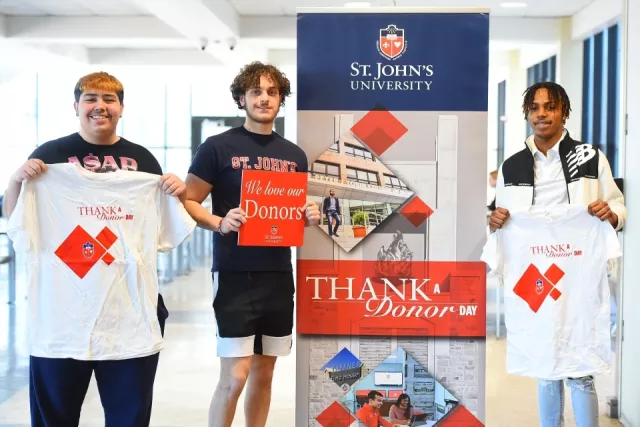 St. John's students holding tshirts for thank a donor day. They are standing in front of a sign that says 'thank a donor'