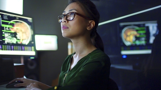 Woman with glasses looking at brain scans on computers