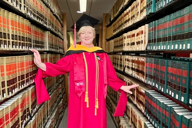Kate Smith in commencement gown in library aisle