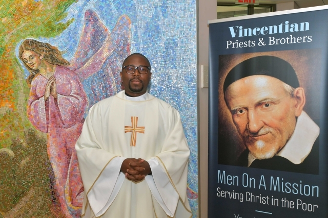 Male standing next to poster featuring St. Vincent de Paul 