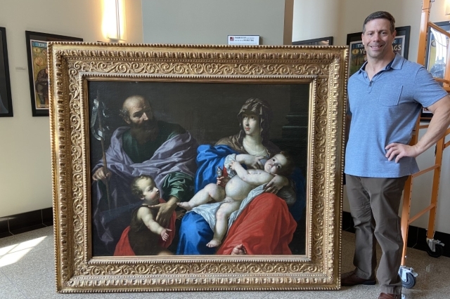 Thomas Ruggio, M.F.A. standing with picture of St John he discovered 