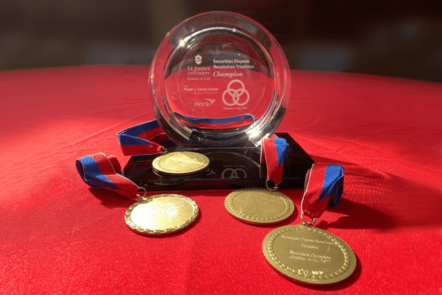 A glass competition trophy sits on a table with several gold medals draped around it.