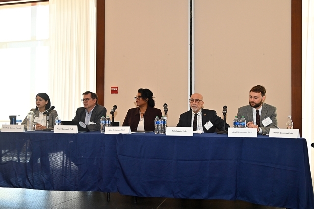 5 panelist sitting at long table infront of audience 