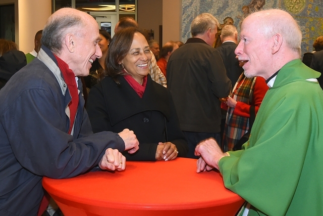 Father Shanely speaking with alumnus couple at hightop table