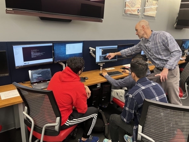 Teacher pointing to computer monitor while students observe in cyber security lab