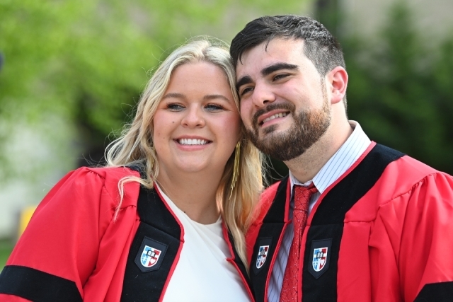 2023 St. John's Law graduates Ashlyn Stone and Matthew Pate pose for a photo in their red and black graduation gowns, leaning their heads together and smiling..
