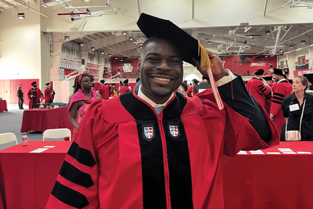 St. John's Law alumnus Rashad Moore, wearing a red graduation gown and a black tam with a gold tassel, smiles.