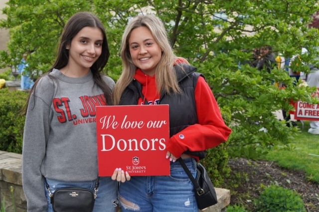 Two female students holding a sign that reads We love our Donors with the St. John's logo