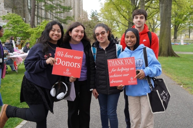 A group of female St. John's Students holding a Thank A Donor Sign on great lawn