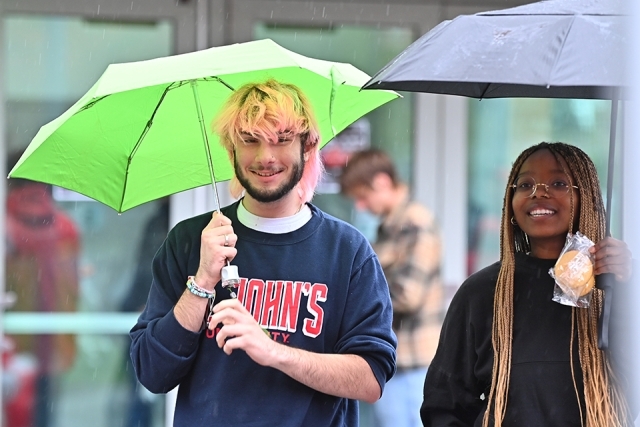 Person in St. John's sweatshirt standing under green umbrella next to a woman under a black umbrella