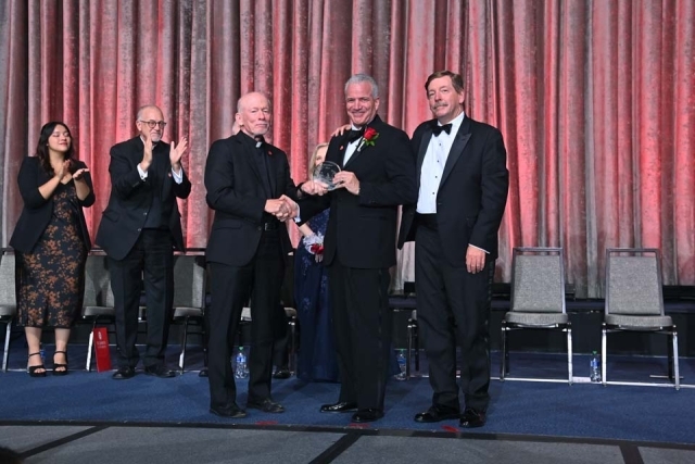 Three males holding award on stage during St. John's President's Dinner
