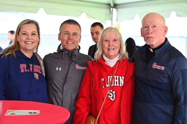 Three people posing with Fr. Shanley for photo during St. John's Homecoming Weekend 2023 