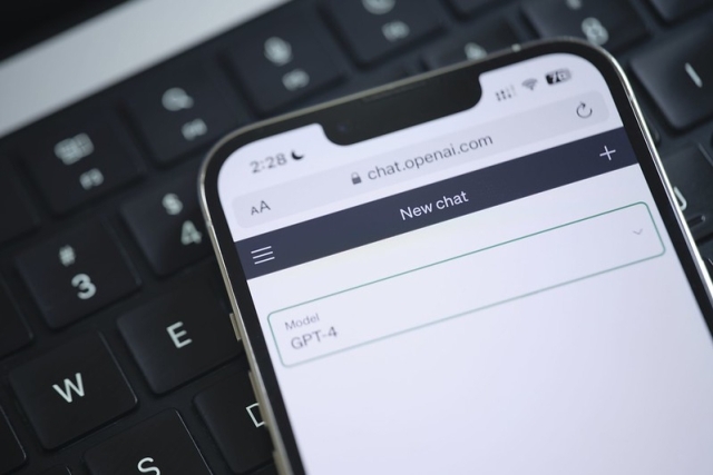 A cell phone being held over a keyboard with ChapGPT on the screen