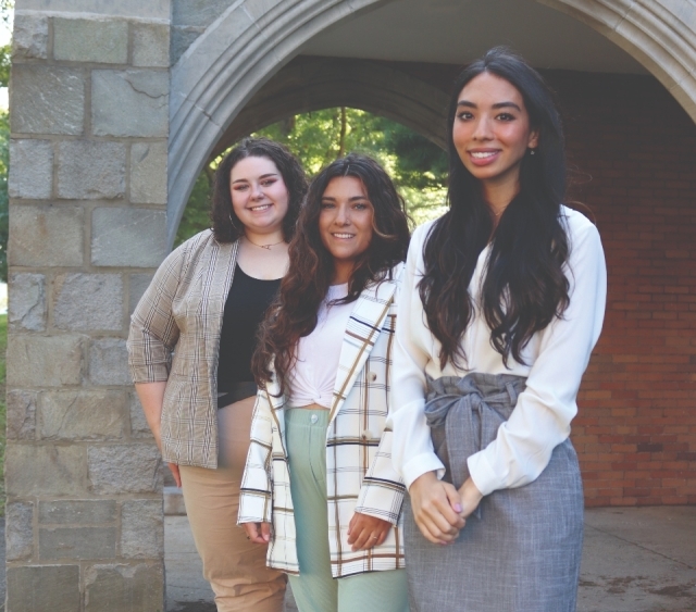 Three Rose DiMartino student fellows stand by a stone arched building entrance.