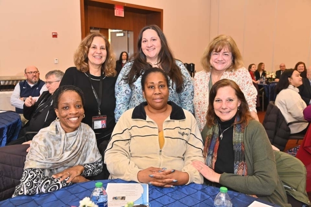 Group of six women pose for a photo at a table