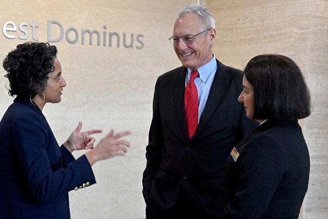 Two women speaking to a man wearing a suit and red tie