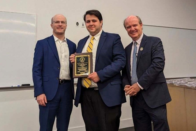 Three men standing and posing with St. Patrick's Day plaque 