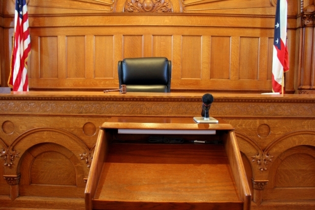 Courtroom judge's bench and chair flanked by American flags with an attorney's lectern in the foreground..