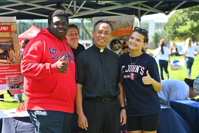 Three students posting with Fr. Tre at the SJU Student Activities Fair