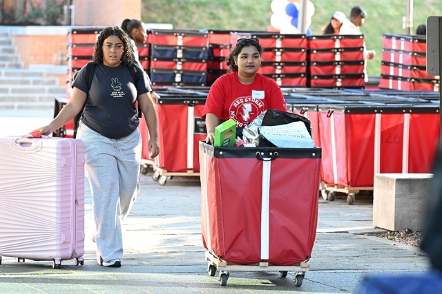 Two females pushing luggage bin cart