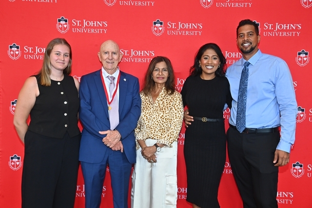 Honoree and four individuals in front of red St. John's step and repeat