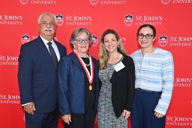 Honoree and three individuals in front of red St. John's step and repeat
