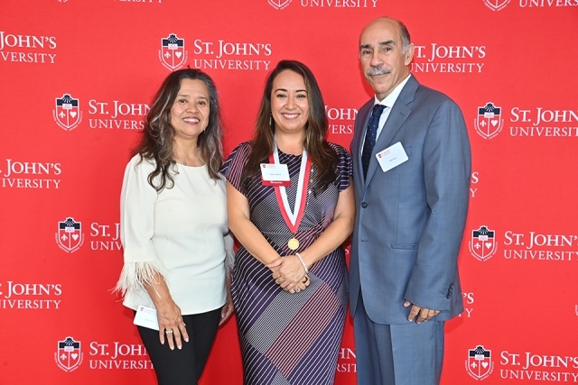 Honoree and two individuals in front of red St. John's step and repeat